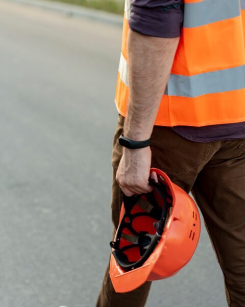 A construction worker in an orange vest and safety helmet walks along a road, highlighting Philippines Construction Safety Standards.