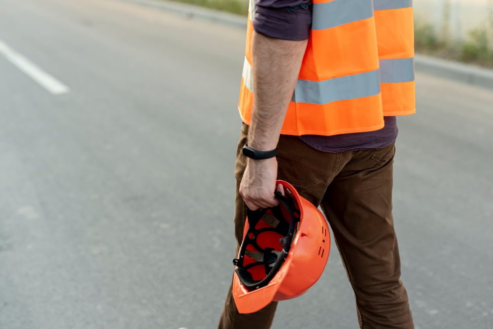 A construction worker in an orange vest and safety helmet walks along a road, highlighting Philippines Construction Safety Standards.