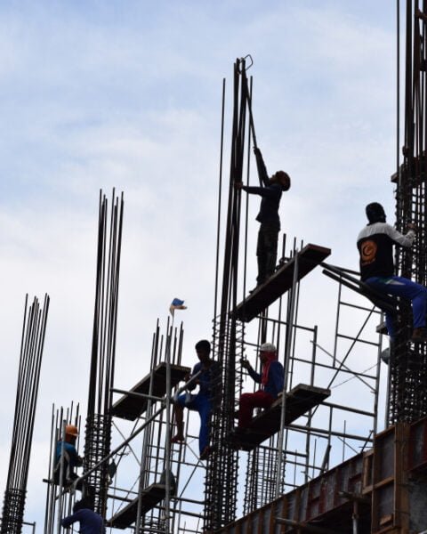 Filipino construction steel-men working joining column steel pieces on board scaffolding pipes on high-rise building, representing the compliance of Philippines Construction Regulations.