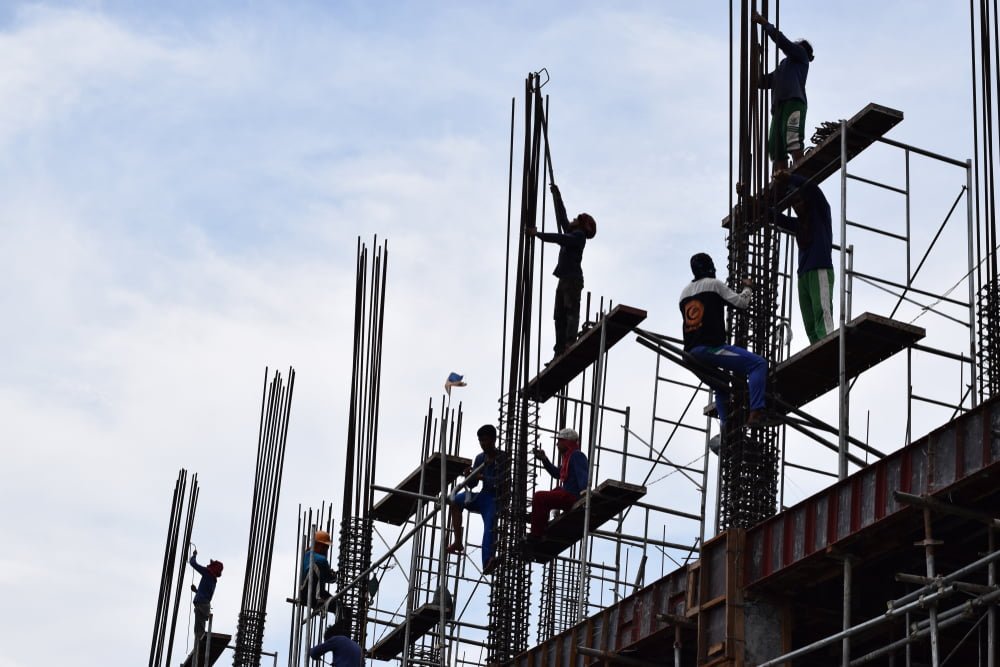 Filipino construction steel-men working joining column steel pieces on board scaffolding pipes on high-rise building, representing the compliance of Philippines Construction Regulations.