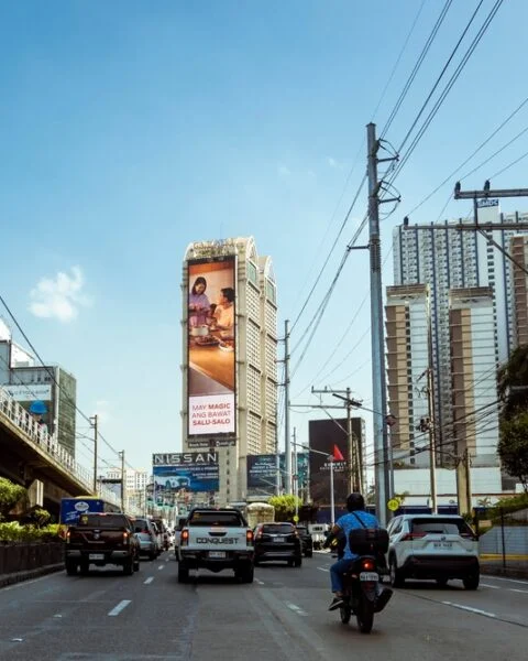 A busy city street in Metro Manila, showcasing heavy traffic and a large billboard displaying vibrant advertisements.