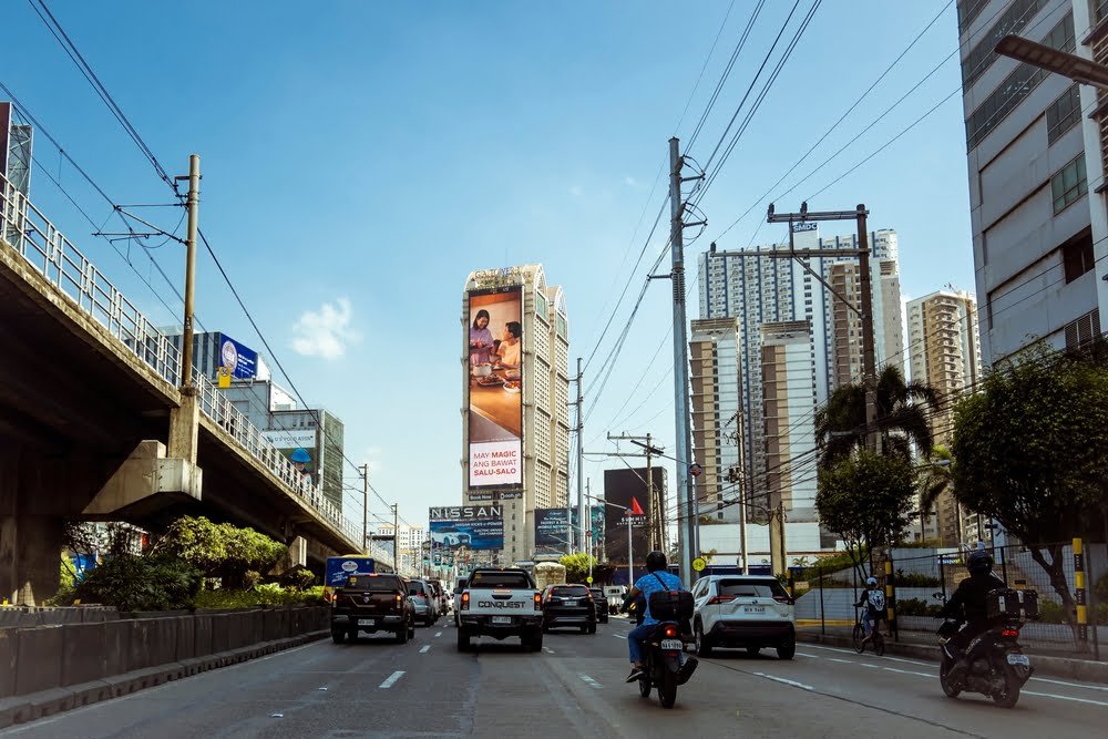 A busy city street in Metro Manila, showcasing heavy traffic and a large billboard displaying vibrant advertisements.