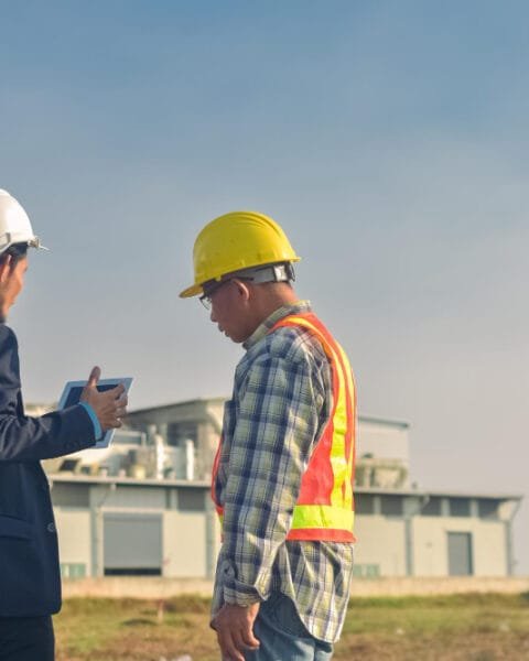 Two construction workers in hard hats discussing Philippines Construction Costs on a worksite.