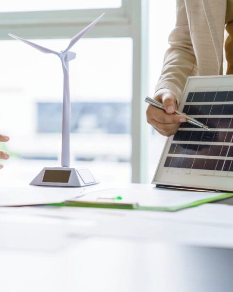 Philippines Renewable Energy in Construction: Professionals discussing renewable energy with a solar panel and wind turbine model on table.