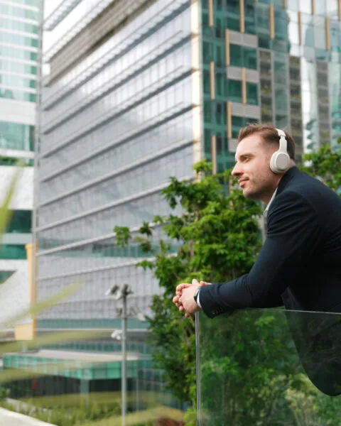 Philippines Green Building Movement: A man in a suit leans against a glass railing, gazing at modern skyscrapers and greenery in an urban setting.