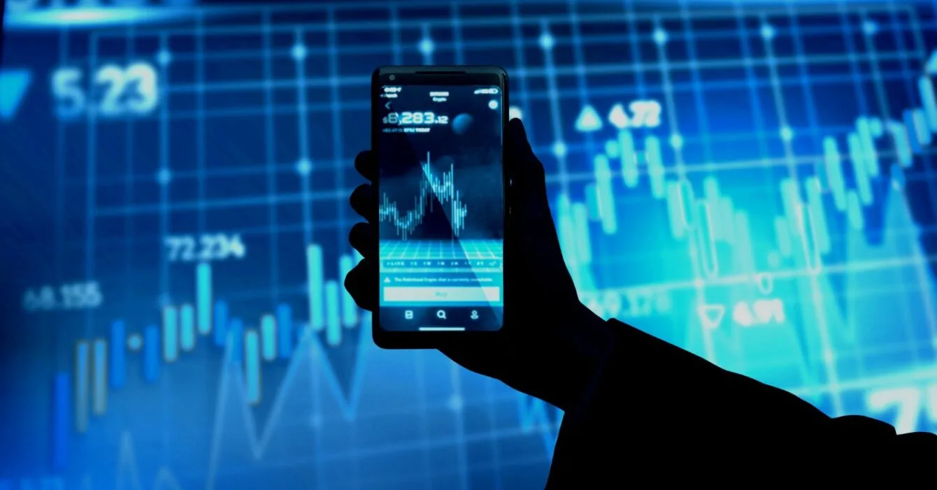 Philippines Fintech Market Expansion: A silhouette hand holding a smartphone displaying a stock market graph, with blue digital data background and financial indicators.