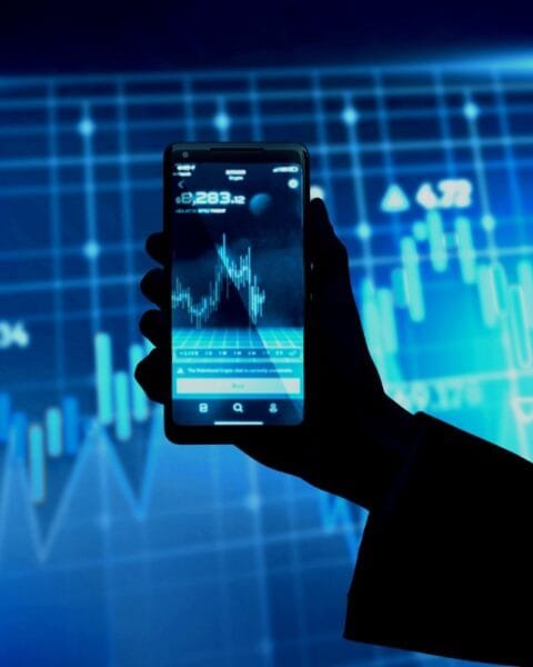 Philippines Fintech Market Expansion: A silhouette hand holding a smartphone displaying a stock market graph, with blue digital data background and financial indicators.