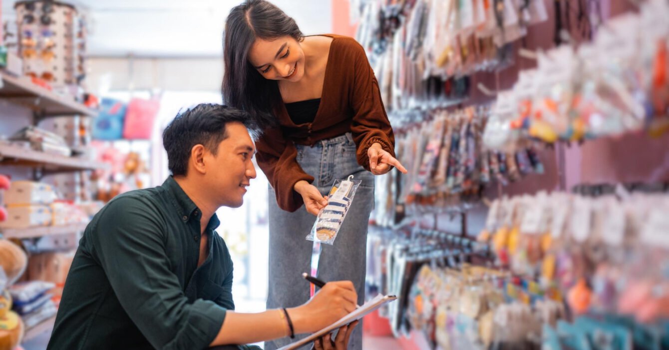 A woman in a brown top shows a product to a man in a green shirt, who is taking notes in a colorful accessories store, representing Philippines Retail Industry Insights.