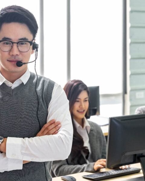 Philippines BPO Industry Outlook - A call center team, with a focus on a confident man in a headset, stands in front of computers and large windows.