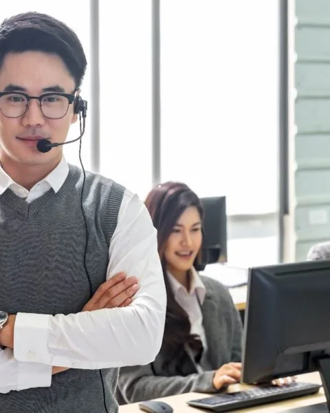 Philippines BPO Industry Outlook - A call center team, with a focus on a confident man in a headset, stands in front of computers and large windows.