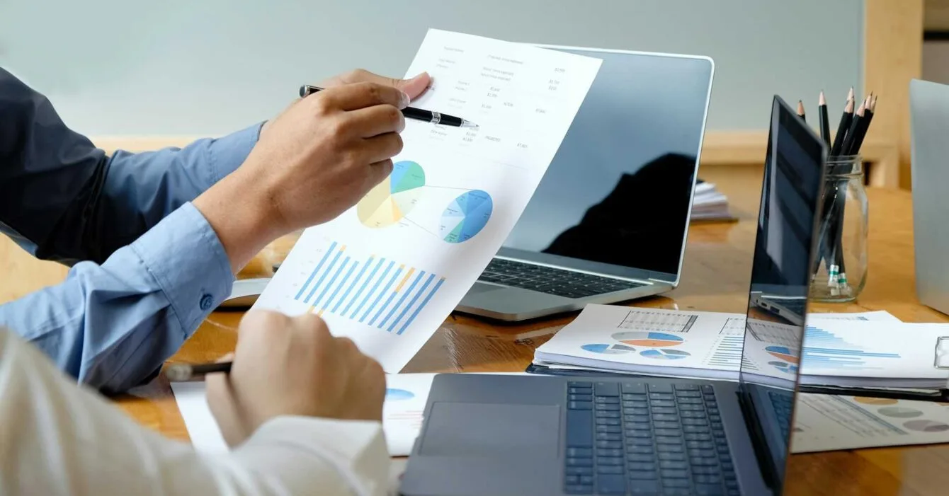 getty-images-D2waESlGhRc-unsplash Philippines Marketing Strategies 2025: Two professionals analyze charts and graphs on paper during a meeting, with laptops and documents on a wooden table.