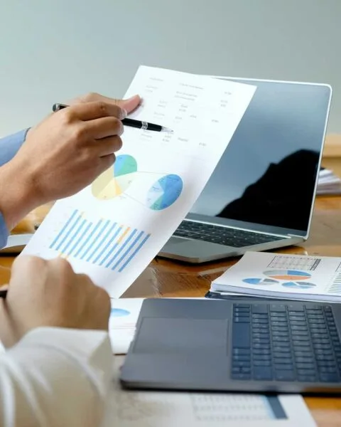 Philippines Marketing Strategies 2025: Two professionals analyze charts and graphs on paper during a meeting, with laptops and documents on a wooden table.