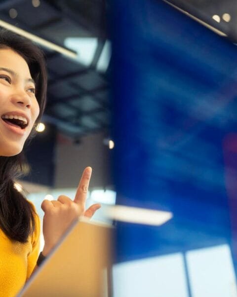 Philippines Telecom Consolidation: An Asian woman in a yellow sweater gestures while speaking on the phone in a modern, well-lit office space.