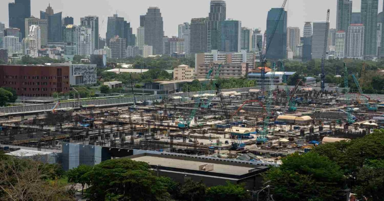 Philippines Infrastructure Development Plans: A large construction site with cranes and scaffolding in the foreground, overlooking a skyline of modern buildings in the background.