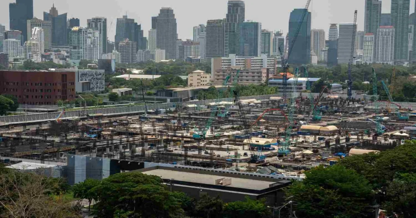 Philippines Infrastructure Development Plans: A large construction site with cranes and scaffolding in the foreground, overlooking a skyline of modern buildings in the background.