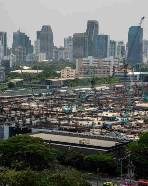 Philippines Infrastructure Development Plans: A large construction site with cranes and scaffolding in the foreground, overlooking a skyline of modern buildings in the background.