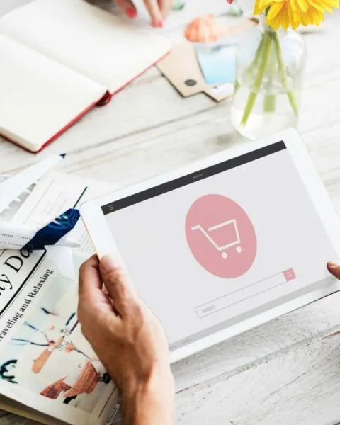 Philippines E-commerce Innovation: A person uses a tablet displaying a shopping cart icon while surrounded by travel-related items and a refreshing drink.