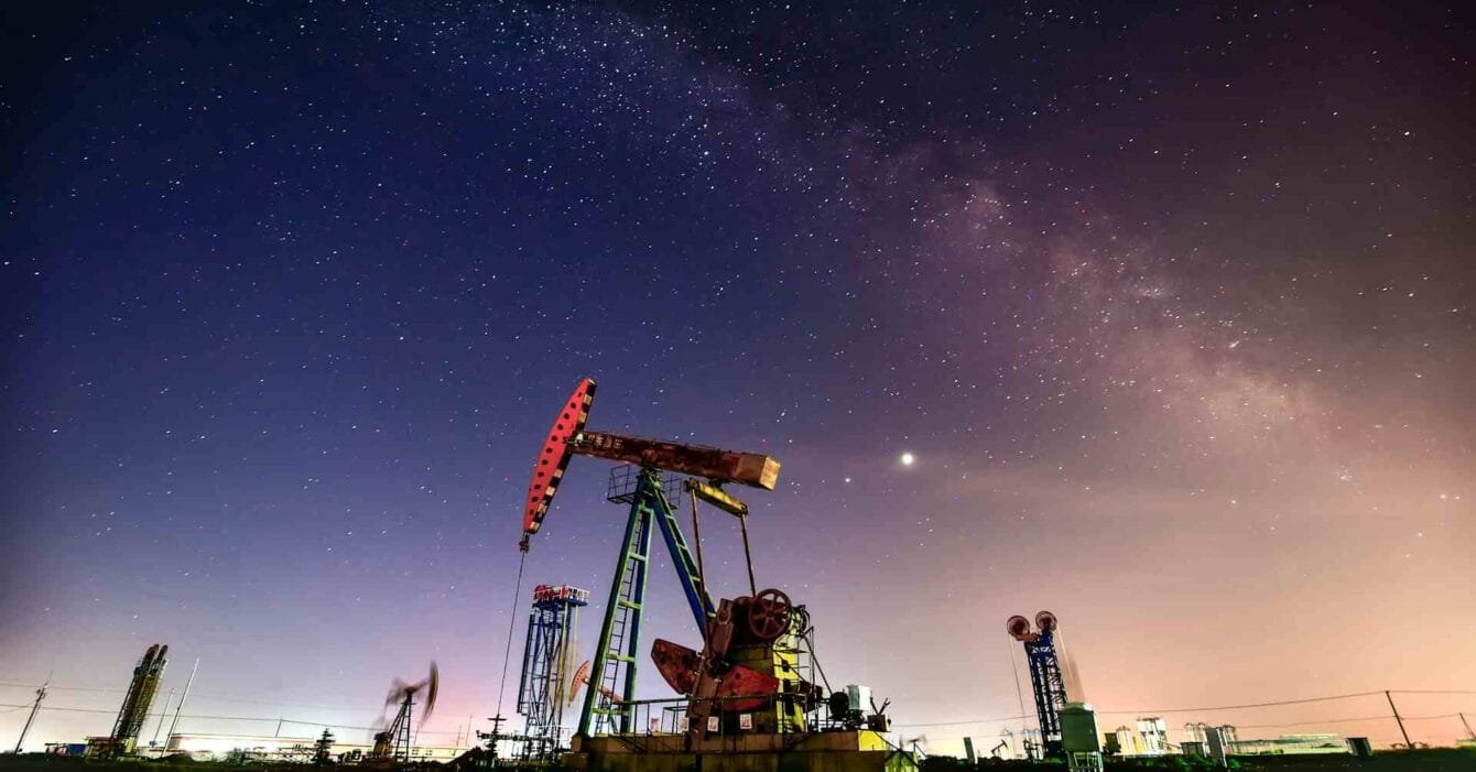 Philippines Oil Price Cut Impact: Night sky filled with stars over an oil pump, reflecting industrial activity under the Milky Way's glow and distant city lights.
