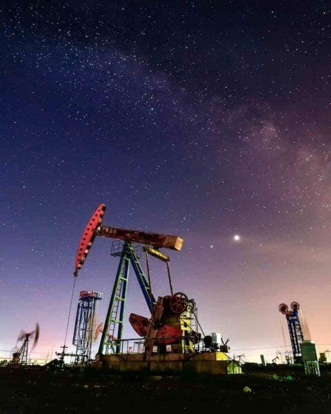 Philippines Oil Price Cut Impact: Night sky filled with stars over an oil pump, reflecting industrial activity under the Milky Way's glow and distant city lights.
