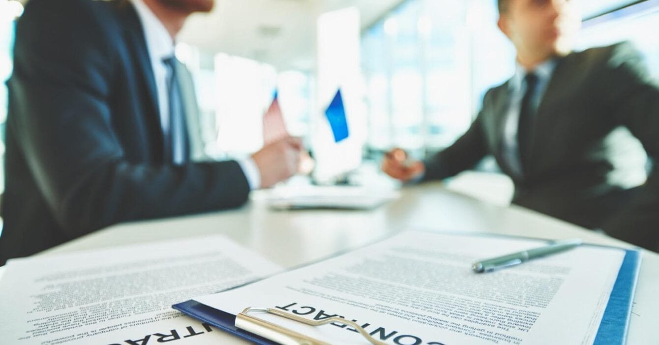 Philippines M&A Regulation Updates: Two business professionals discuss a contract in a modern office setting, with documents and pens arranged on the table.