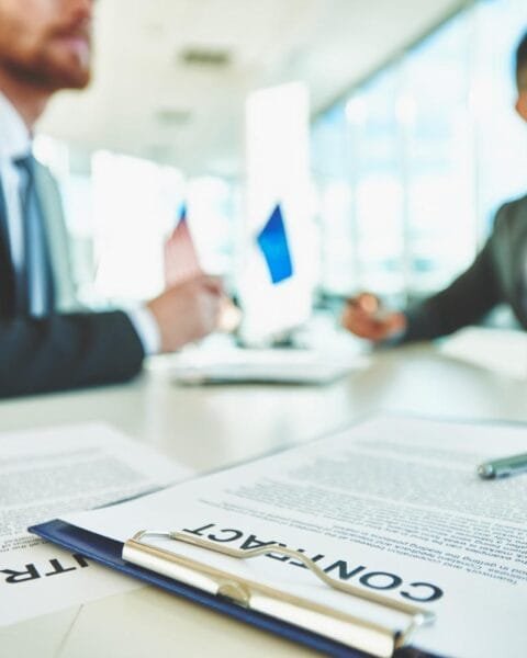 Philippines M&A Regulation Updates: Two business professionals discuss a contract in a modern office setting, with documents and pens arranged on the table.