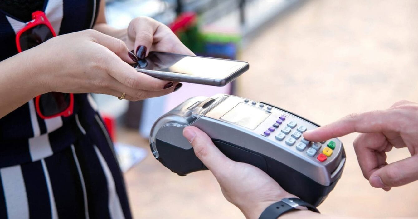 getty-images-ZaimuWZbrEg-unsplash Philippines Mobile Money Trends: A person holding a smartphone prepares to make a contactless payment using a card reader held by another person.
