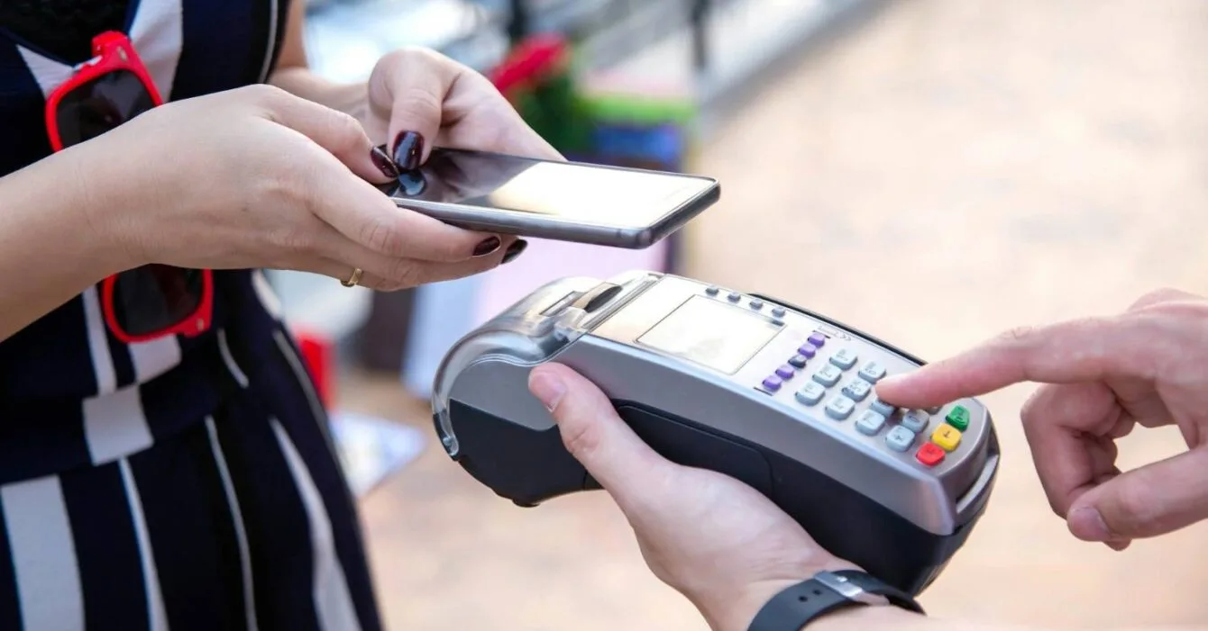 Philippines Mobile Money Trends: A person holding a smartphone prepares to make a contactless payment using a card reader held by another person.