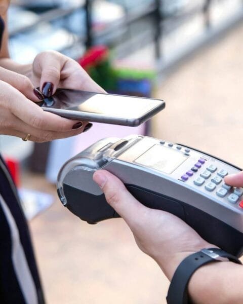 Philippines Mobile Money Trends: A person holding a smartphone prepares to make a contactless payment using a card reader held by another person.