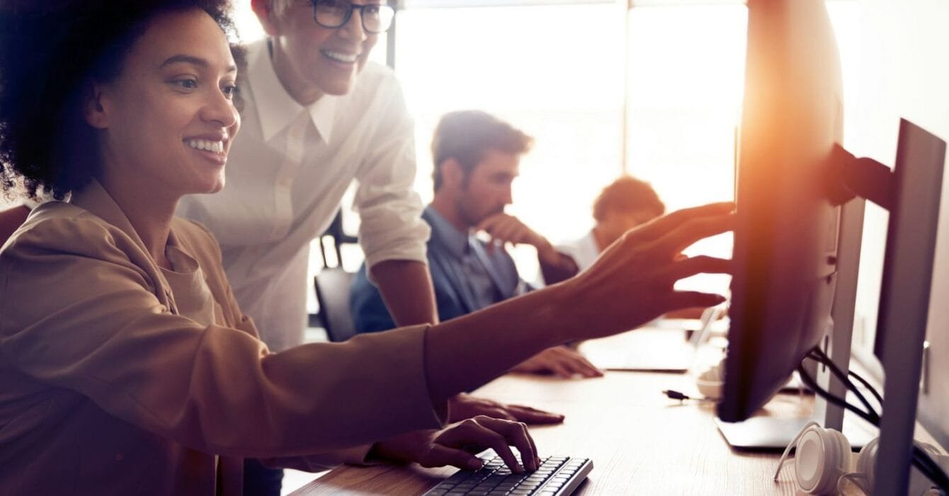 Philippines BPO trends 2025: A group of people collaborate around a desk with computers, one person points to a screen while another types on the keyboard.