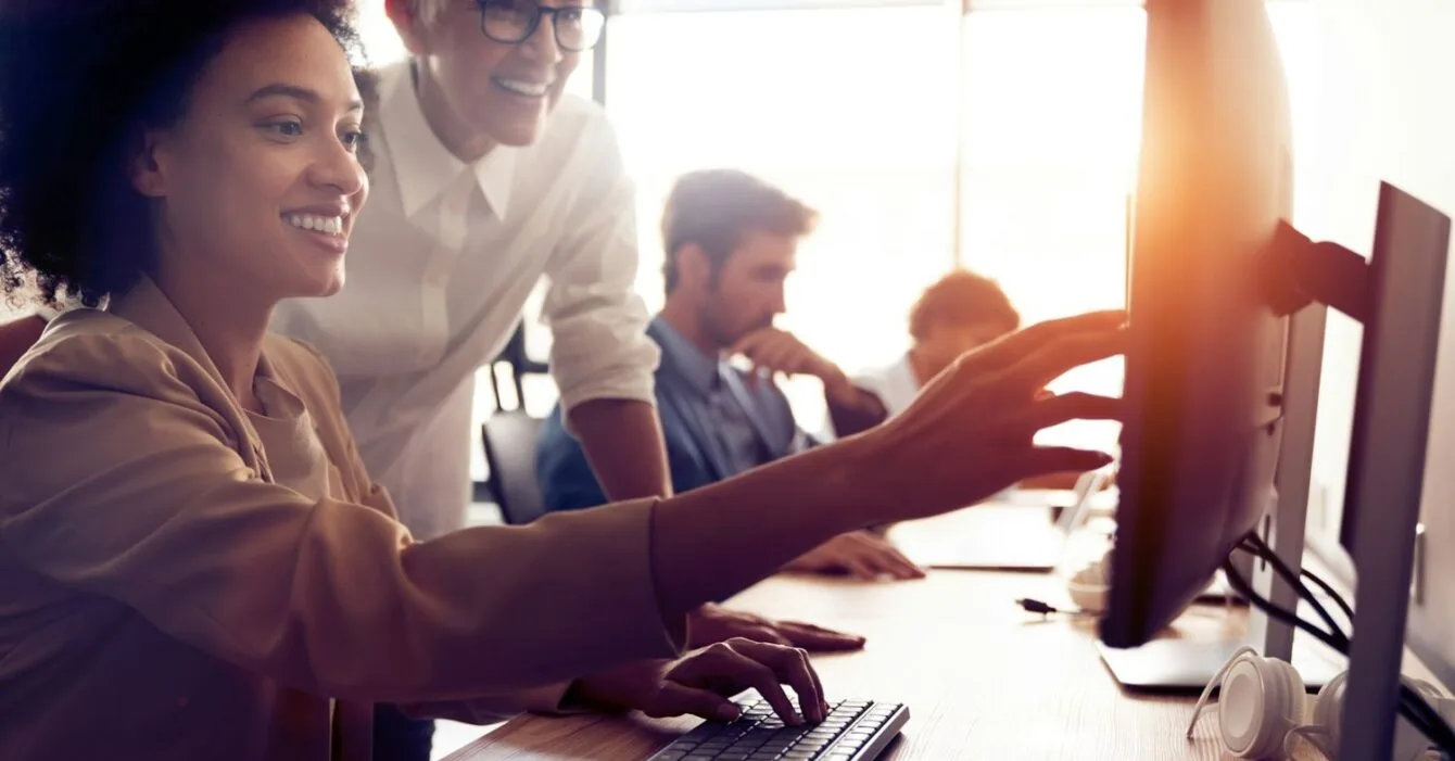 getty-images-I3KCnSMAgGI-unsplash Philippines BPO trends 2025: A group of people collaborate around a desk with computers, one person points to a screen while another types on the keyboard.