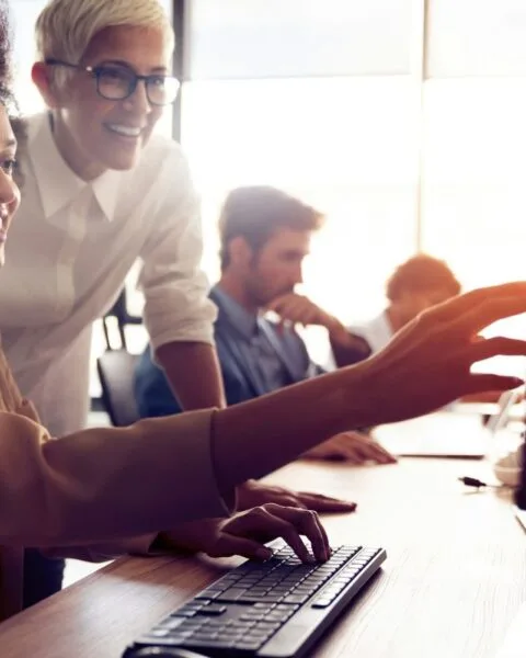 Philippines BPO trends 2025: A group of people collaborate around a desk with computers, one person points to a screen while another types on the keyboard.
