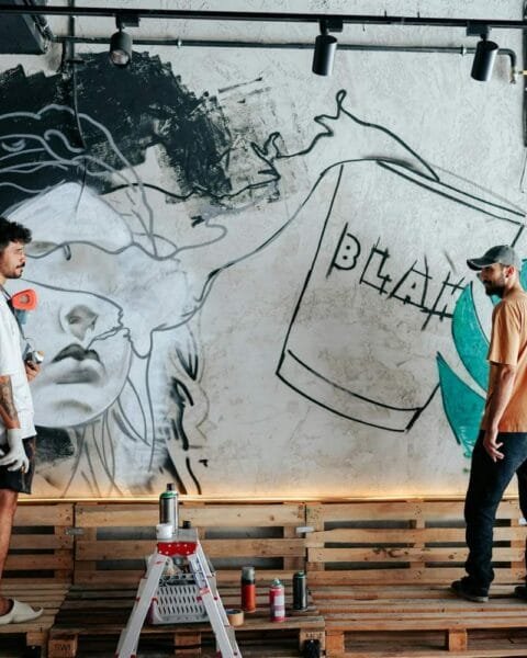 Philippines creative economy 2026: Two artists work on a mural featuring a stylized face and abstract elements on a textured wall, surrounded by paint supplies.